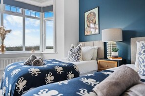A bedroom with two beds, a window, a lamp, and a painting on the wall.