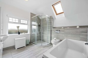 Une salle de bain moderne dotée d’une douche à parois de verre, d’une baignoire sur pieds et d’une fenêtre en verre dépoli.