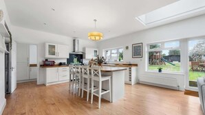 A spacious kitchen with a central island, white cabinetry, and a large window overlooking a garden. - Cosy 5BRLuxe House, w/Games Room, Great for Groups (Widley)