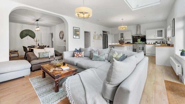 A modern living room with a sofa, coffee table, and a dining area with a kitchen in the background. - Cosy 5BRLuxe House, w/Games Room, Great for Groups (Widley)