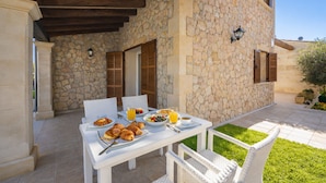 An outdoor dining area with stone walls, wooden beams, and white furniture.