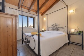 Un lit à baldaquin avec une couvre-lit blanche, une armoire en bois, une fenêtre avec des rideaux et un luminaire fixé au mur.