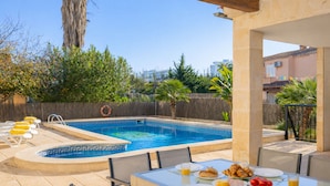 A poolside dining area with a table set for breakfast, a hot tub, and a view of the surrounding area.