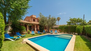 Una piscina rectangular con borde de azulejos, rodeada por un césped cuidado y sillones de descanso azules.