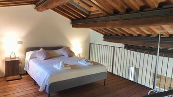 A bedroom with a wooden ceiling, a bed with white linens, and a nightstand with a lamp.