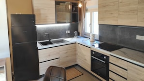 Une cuisine de taille réduite, avec un réfrigérateur noir, un évier, une cuisinière et des placards en bois.