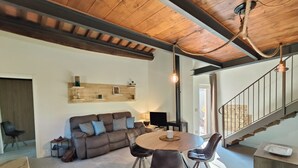 Un salon moderne avec un plafond en bois, un canapé marron agrémenté de coussins, une table ronde en bois entourée de chaises et un escalier doté d’une rampe en métal.