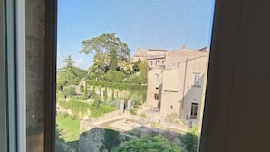 Une vue à travers une fenêtre donnant sur une cour intérieure avec un bâtiment, des arbres et une petite construction.