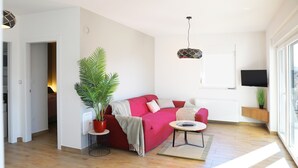 Una sala de estar moderna con un sofá rojo, una mesa de centro, una planta en maceta y un televisor montado en la pared.