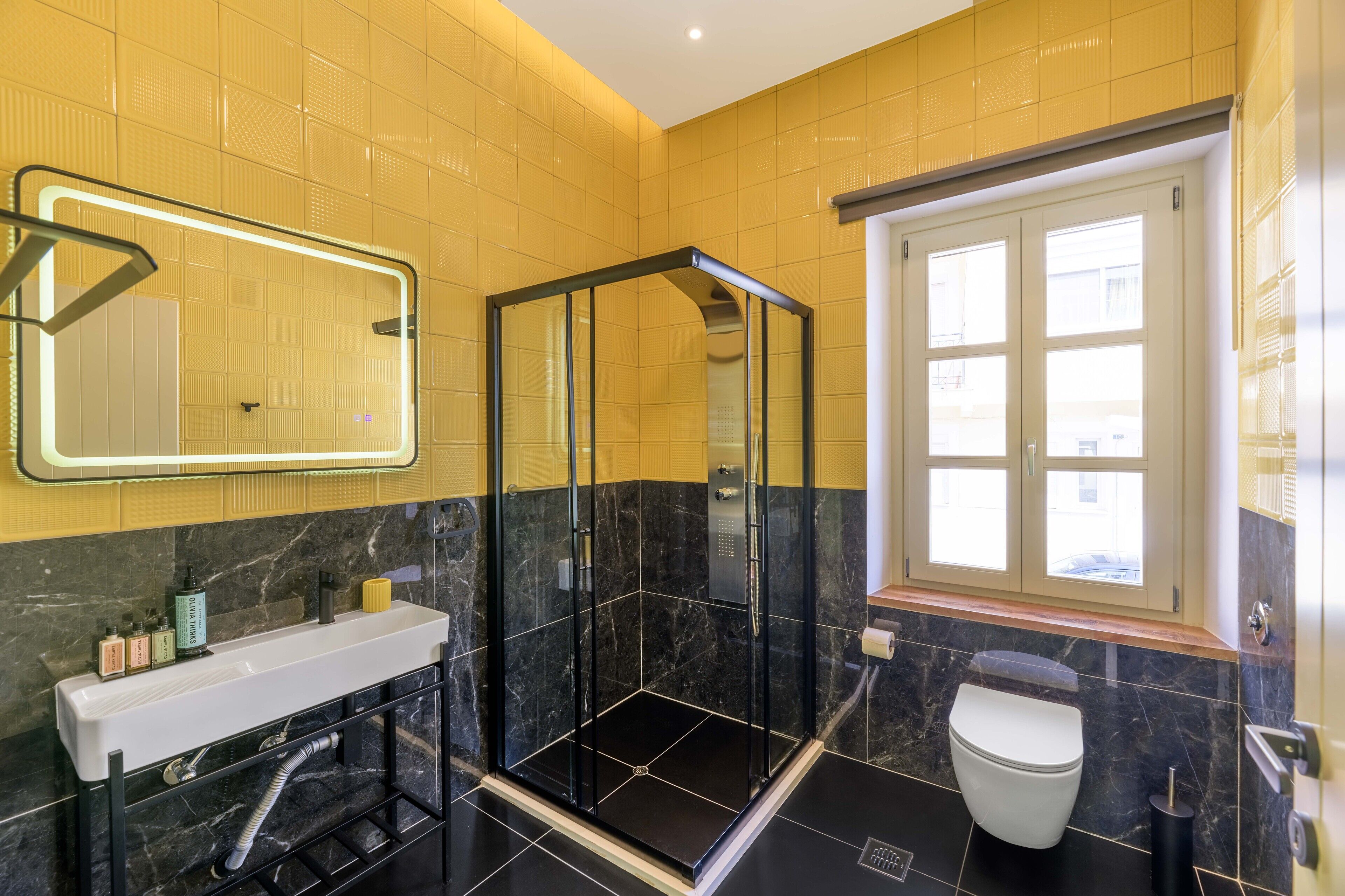 Een moderne badkamer met een douchecabine van glas, een witte wastafel en een toilet.