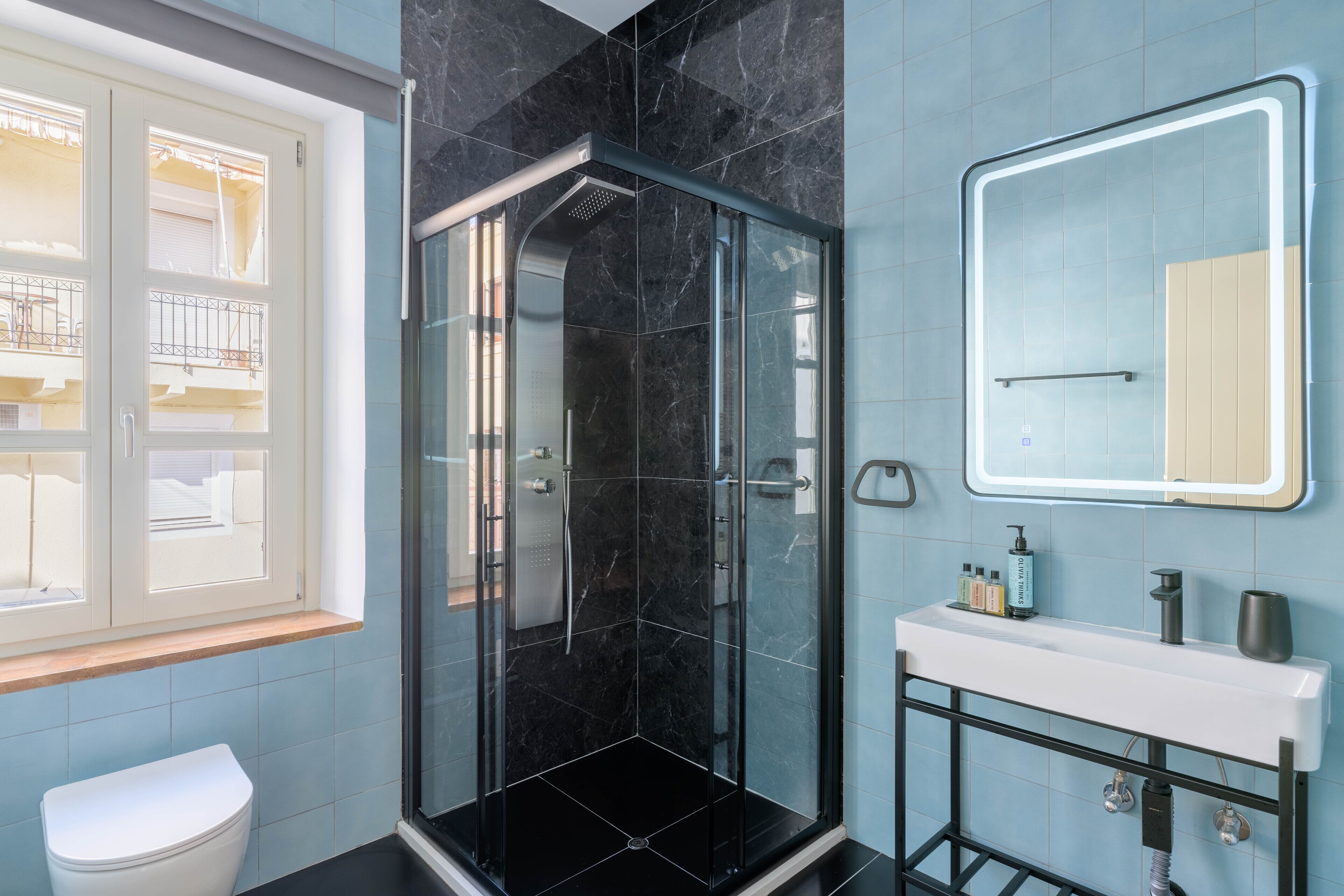 A modern bathroom with a glass-enclosed shower, a white sink, and a mirror with a lighted frame.