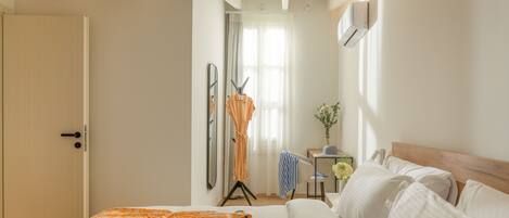 A hotel room with a bed, a desk, a chair, a mirror, and a window with curtains.