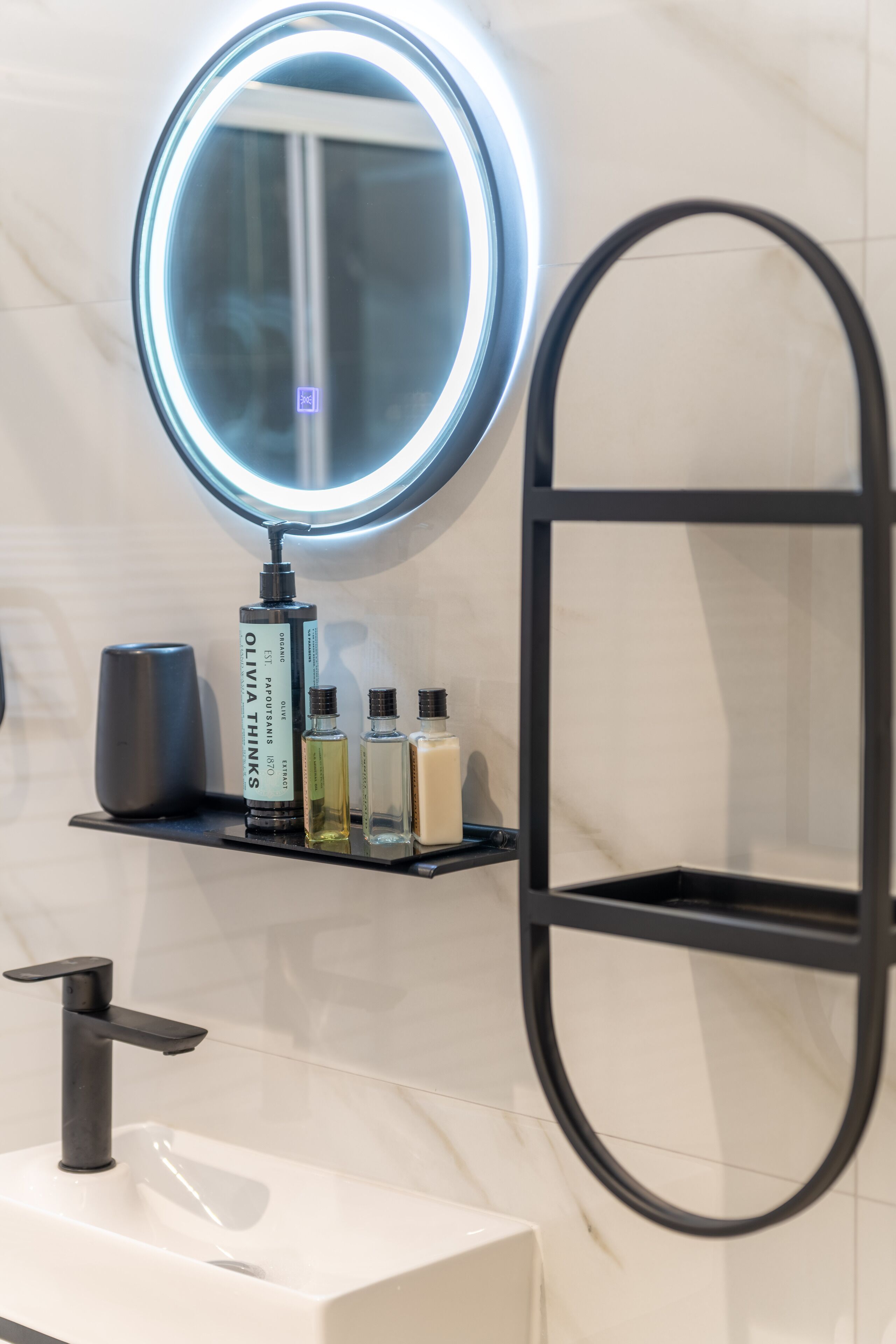 A bathroom with a round mirror, a black shelf with toiletries, and a white sink.
