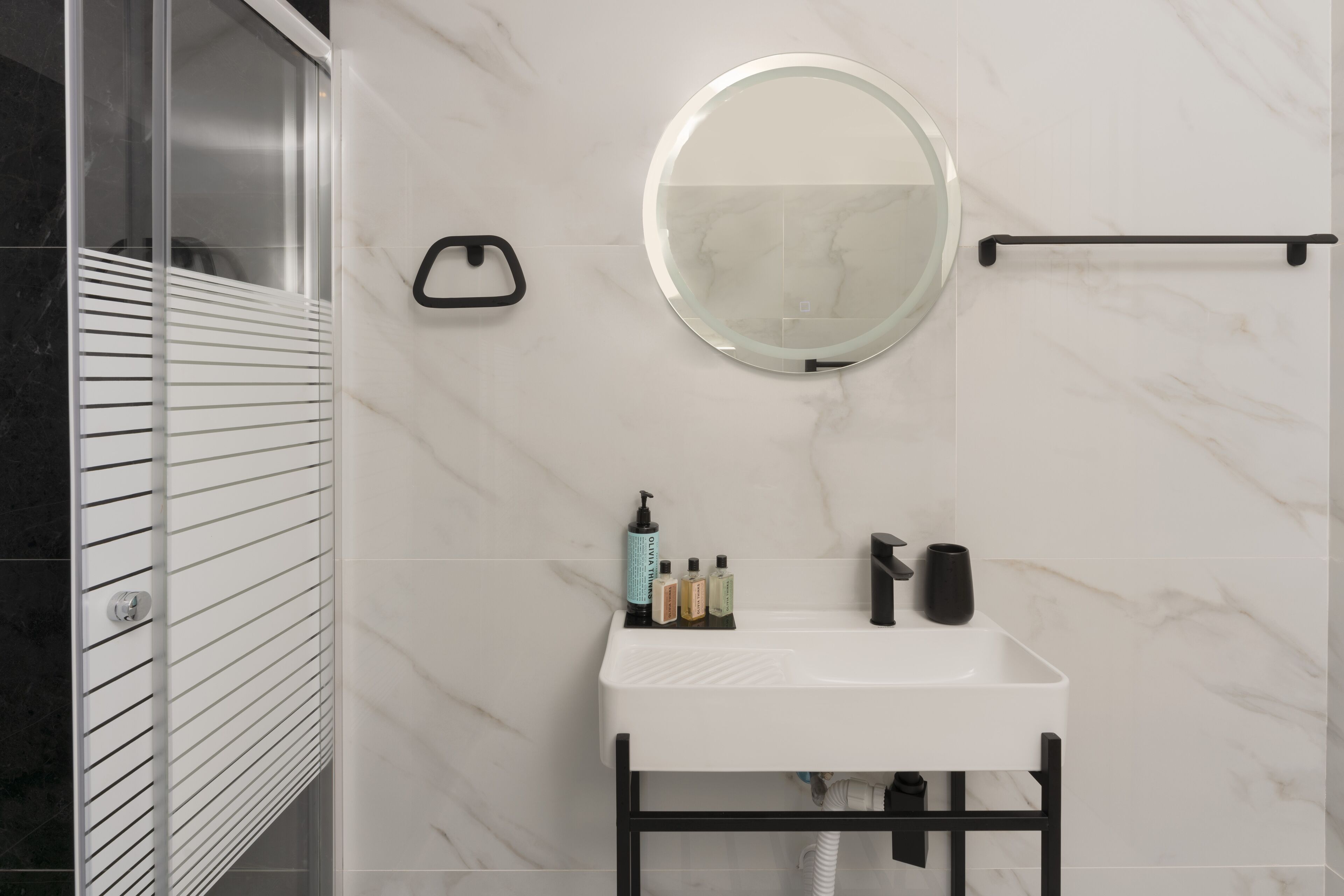 A bathroom with a white sink, a round mirror, and a towel rack.