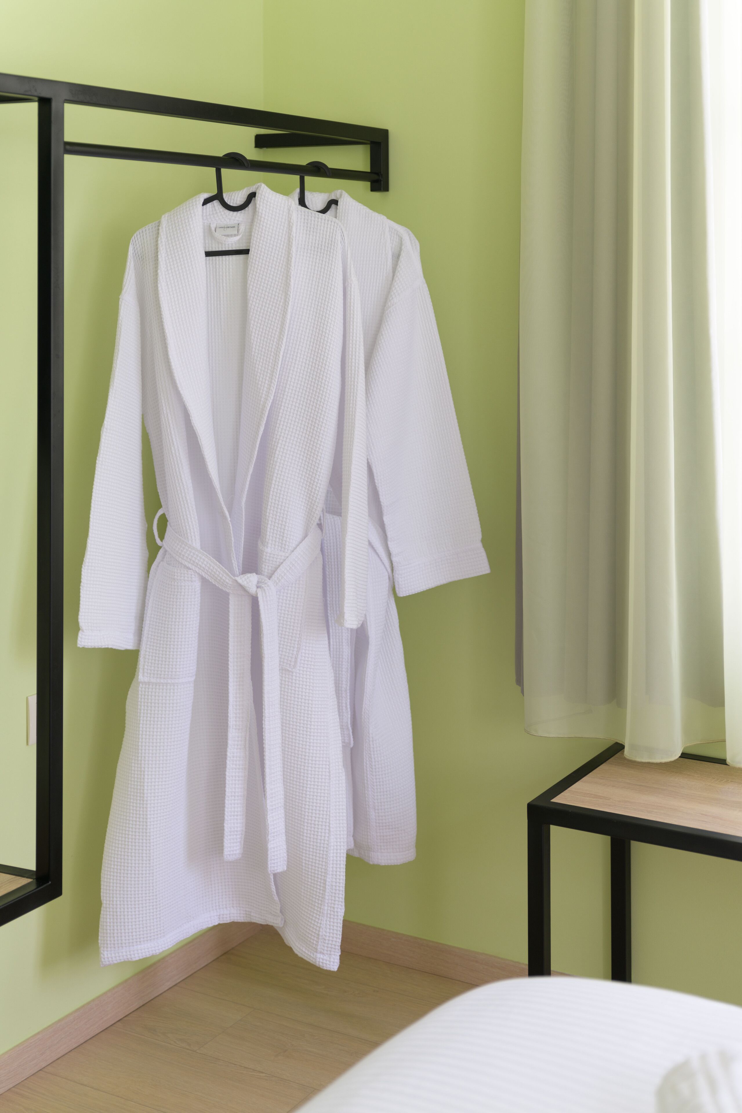 A white bathrobe hanging on a black hanger in a room with a green wall and a wooden floor.
