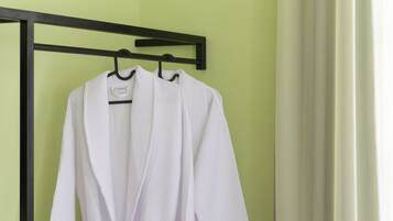 A white bathrobe hanging on a black hanger in a room with a green wall and a wooden floor.