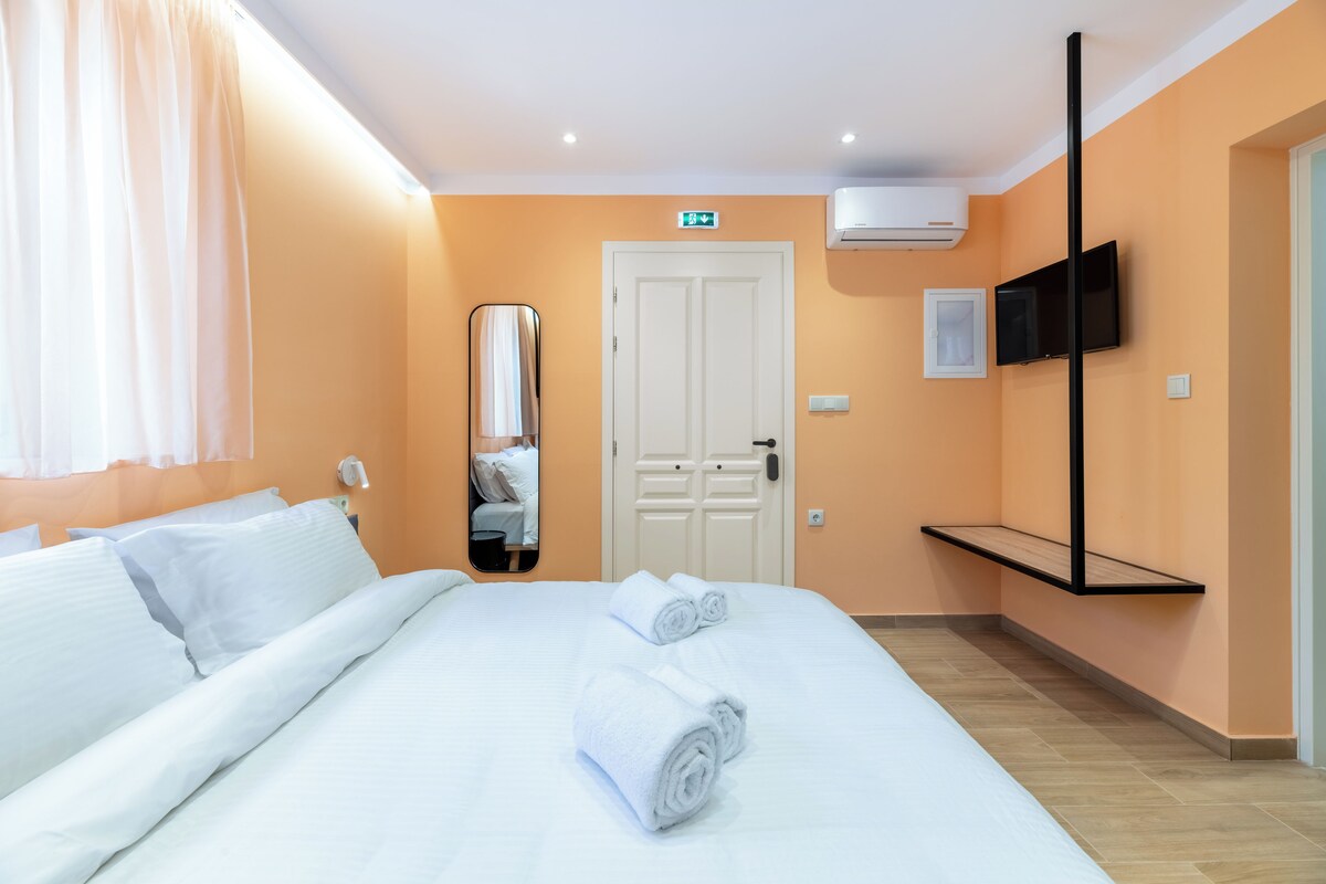 Una habitación de hotel con cama, ropa de cama blanca, un espejo, un televisor y una puerta con letrero de salida.