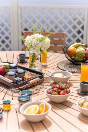 Una mesa de desayuno con diferentes alimentos, un jarrón con flores y vistas al cielo.