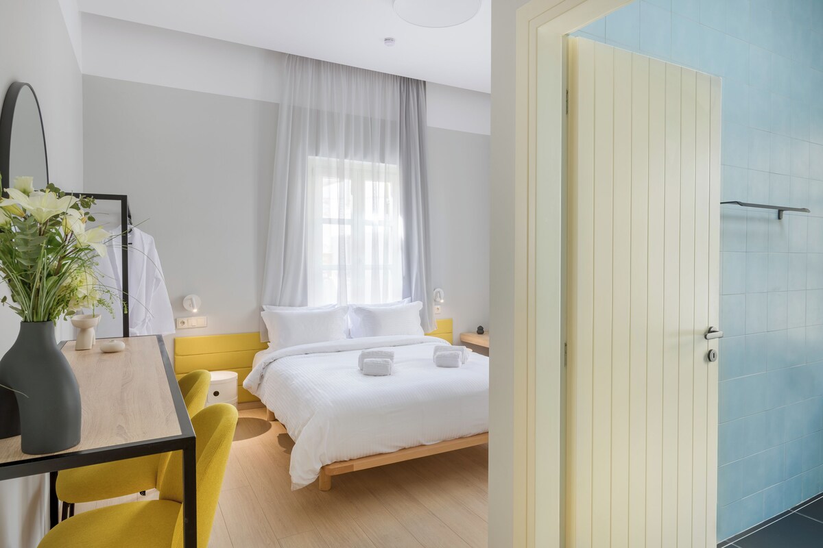 Un dormitorio moderno con una cama de madera, una mesita de noche con lámpara y una ventana con cortinas de gasa.
