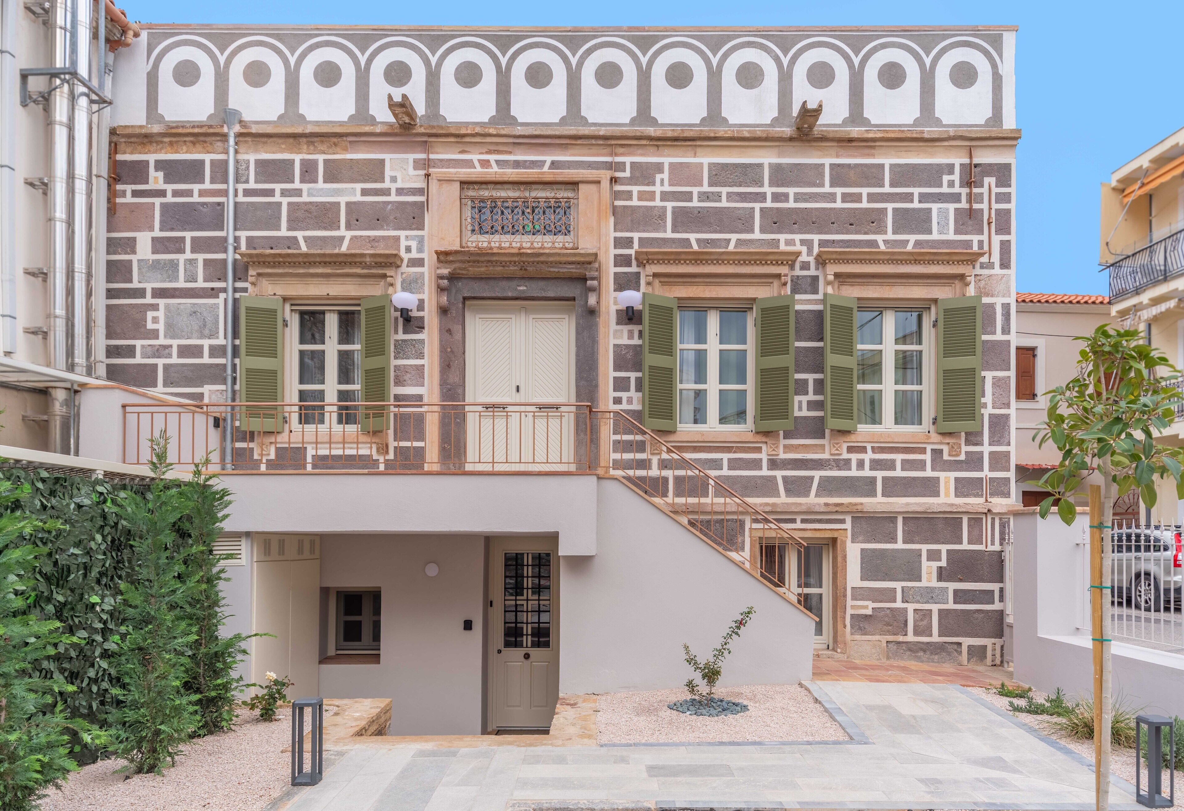 A two-story building with a stone facade, green shutters, and a balcony.