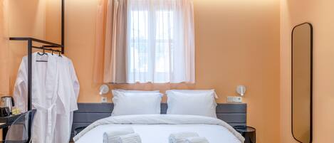 A hotel room with a bed, two bedside tables, a desk with a chair, a mirror, and a window with curtains.