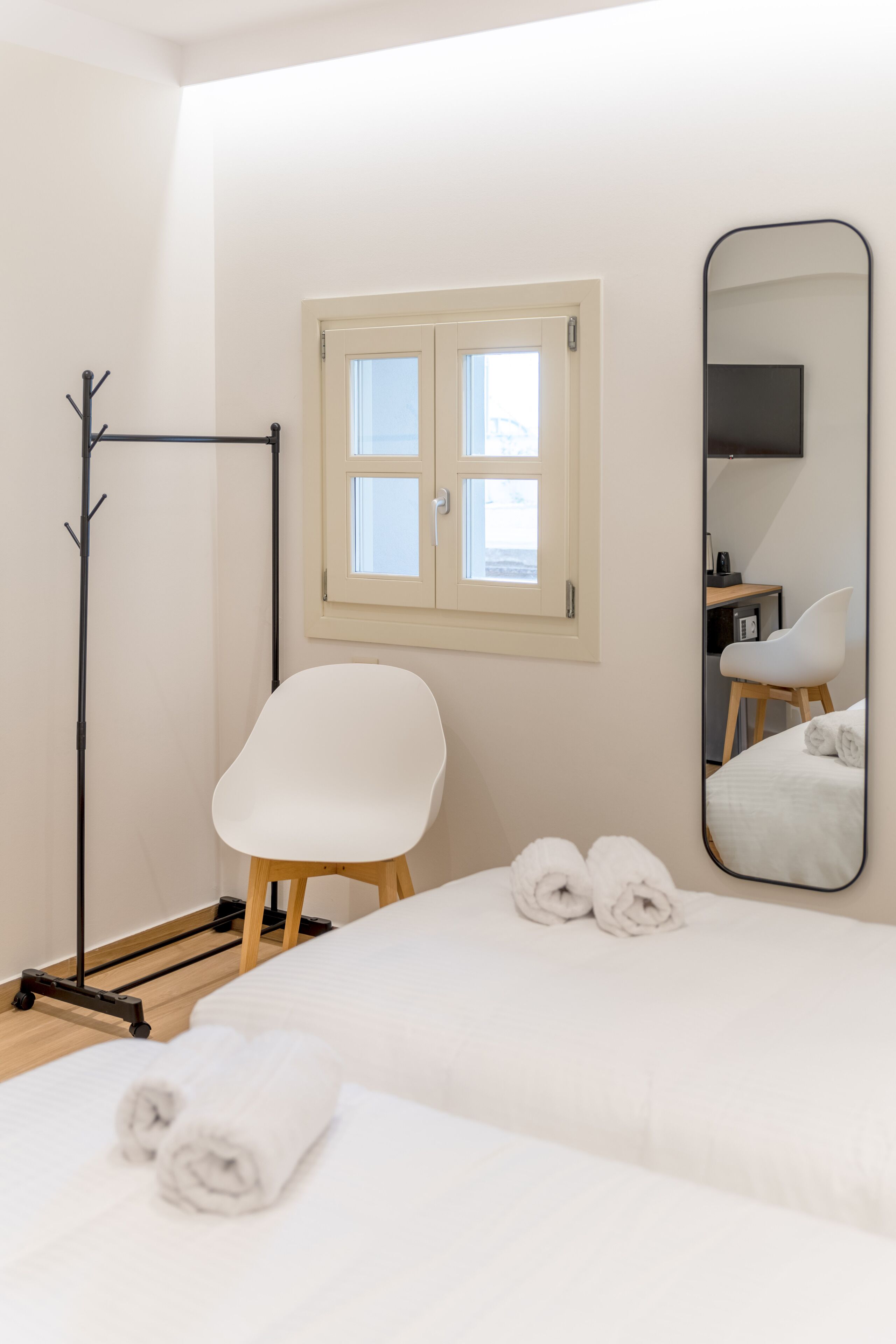 A hotel room with a bed, a white chair, a mirror, and a window.