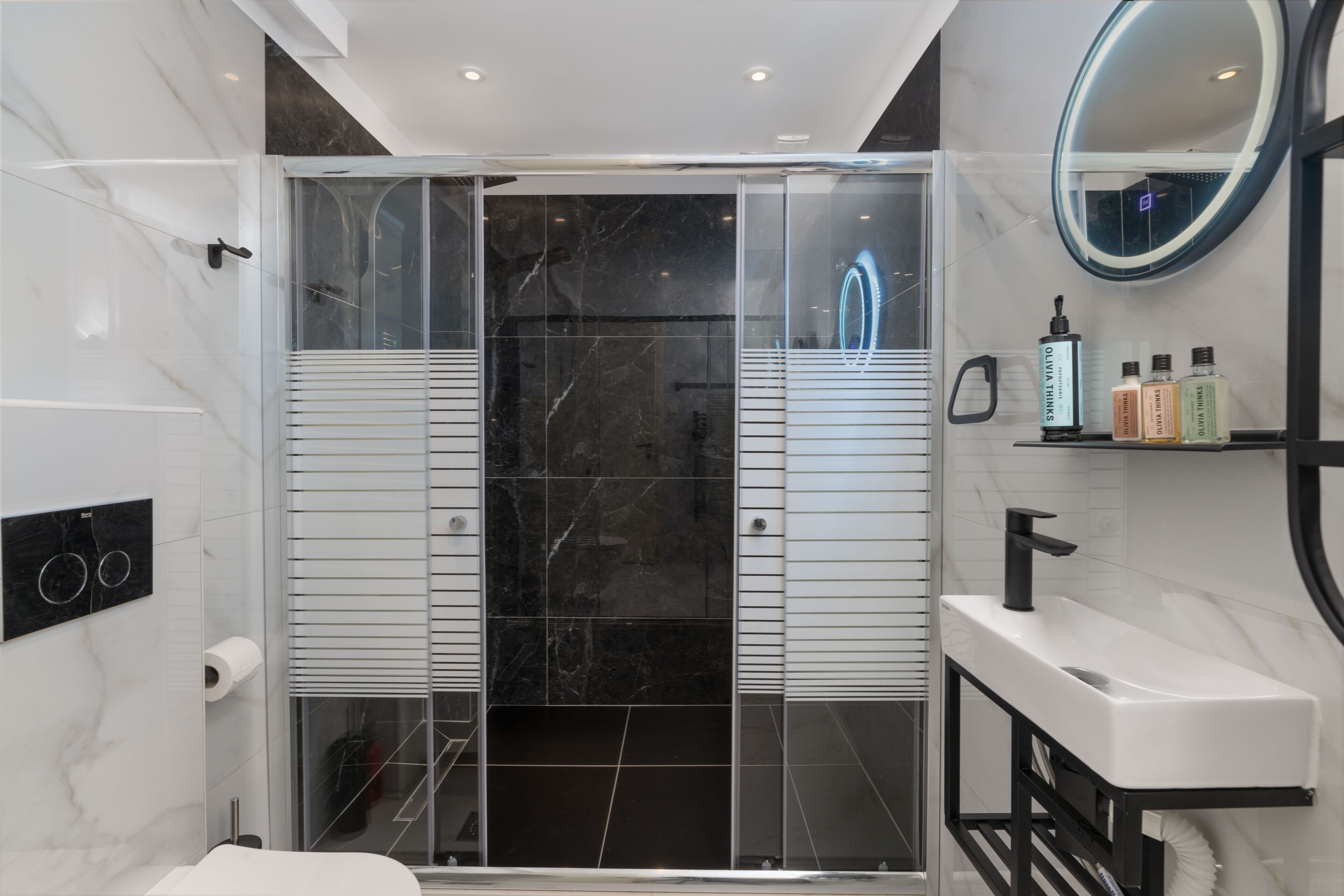 A modern bathroom with a glass-enclosed shower, a white sink, and a mirror with a neon light.