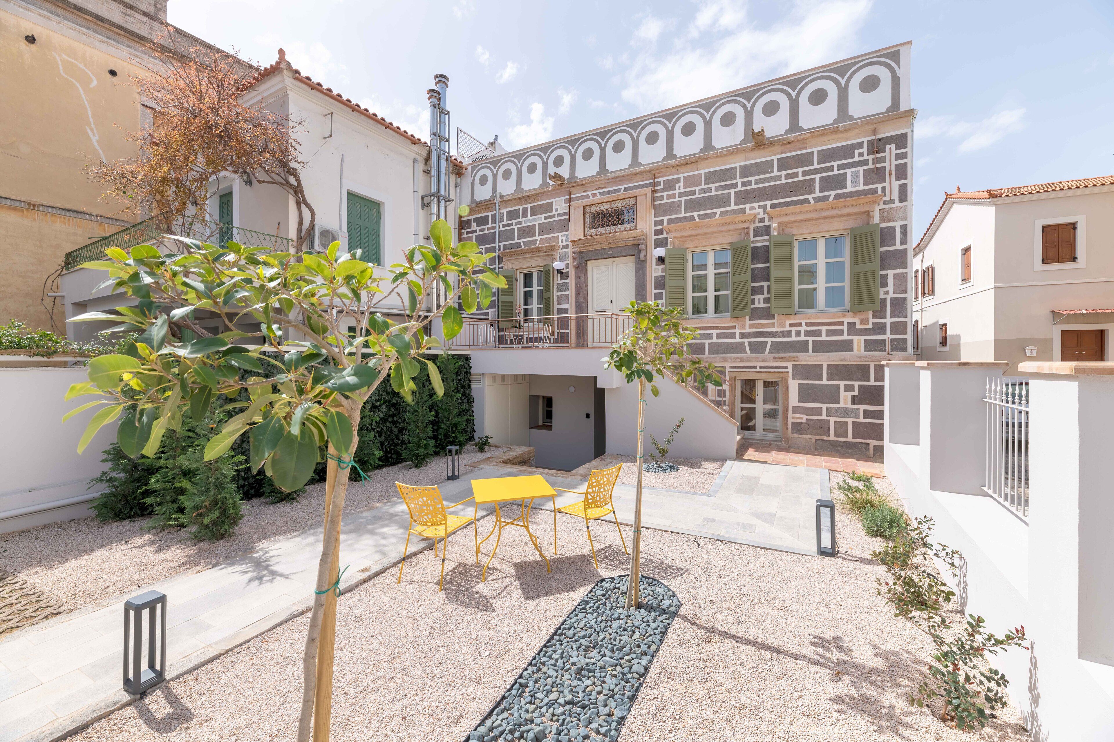 A courtyard with a yellow table and chairs, surrounded by buildings with stone and brick facades.