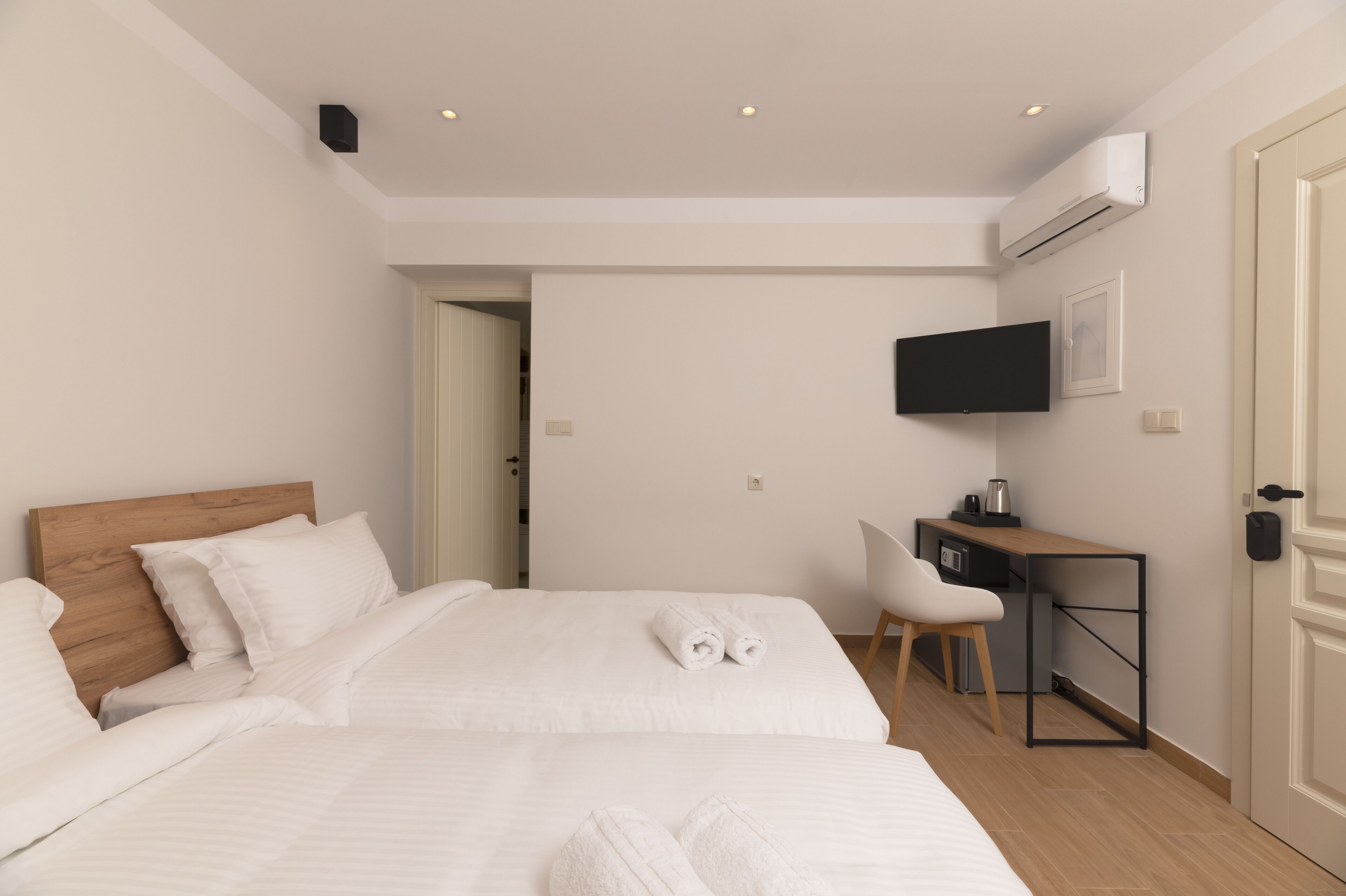 A hotel room with two beds, a desk, a chair, a flat-screen TV, and an air conditioning unit.
