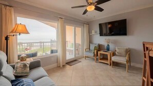 A living room with a sofa, a small table, two chairs, a ceiling fan, and a TV mounted on the wall. - Beachfront resort style in Galveston - 3 Pools - Pet Friendly! (Galveston)