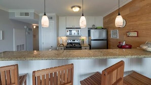 A kitchen with granite countertops, wooden chairs, a stainless steel refrigerator, and pendant lights. - Beachfront resort style in Galveston - 3 Pools - Pet Friendly! (Galveston)