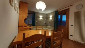 A dining area with a wooden table and chairs, a pendant light, and a window with curtains.