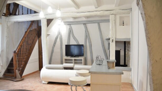 Ein gemütliches Wohnzimmer mit einer Holztreppe, einem Flachbildfernseher, einem weißen Sofa und einer kleinen Bar.
