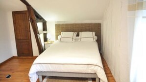 Ein Schlafzimmer mit Holzboden, einem Bett mit weißer Bettwäsche, einem Holzschrank und einer schrägen Decke.