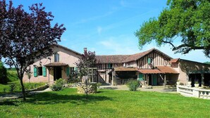 Ein traditionelles, zweistöckiges Haus mit Steinfundament, einem Ziegeldach und einem gepflegten Garten mit Steinmauer und kleinem Baum.