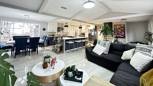 A spacious living room with a black sofa, a coffee table, and a dining area with chairs and a table. - Pet Friendly Suburban Retreat: Modern Comforts for Families w/ firepit (Marietta)