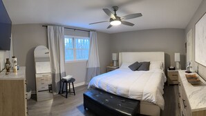 A bedroom with a bed, bedside tables, a mirror, a ceiling fan, and a window with curtains. - Pet Friendly Suburban Retreat: Modern Comforts for Families w/ firepit (Marietta)