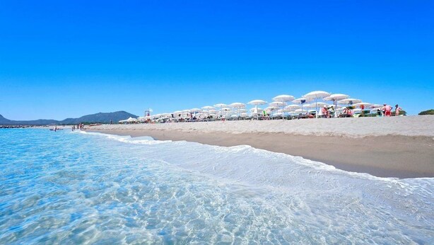 A beach with clear blue water, white sand, and umbrellas. - Villaggio Colostrai (Muravera)