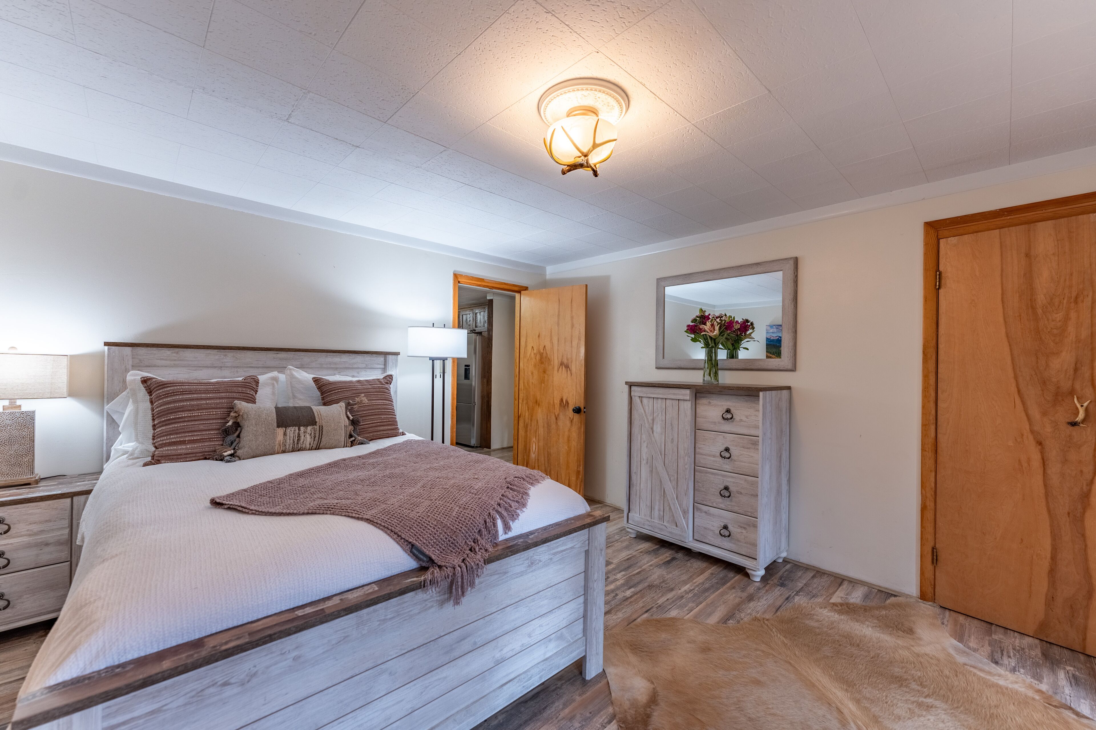 A bedroom with a wooden bed, a nightstand, a dresser, a mirror, and a wooden door.