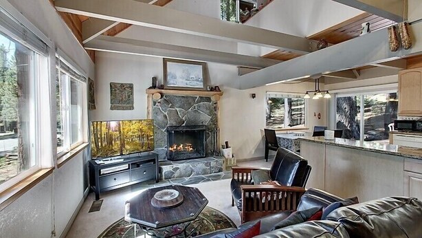 A modern living room with a stone fireplace, a dining area, and a kitchen with wooden cabinets.
