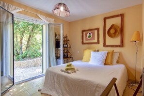 Ein Schlafzimmer mit Bett, Fenster mit Blick auf Bäume, einer Hängelampe und einer Stehlampe.