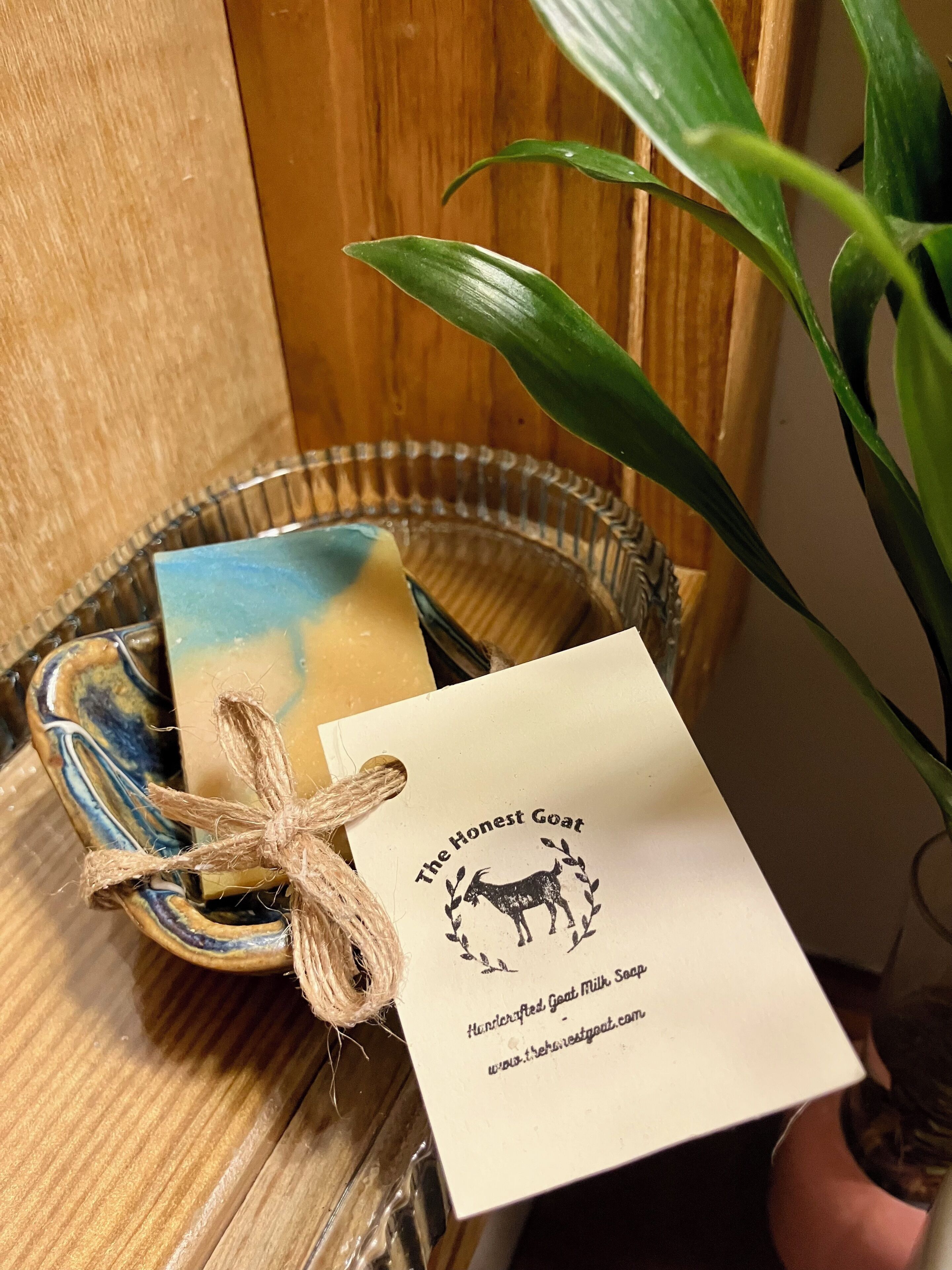 A wooden surface with a glass bowl containing a soap bar and a tag.