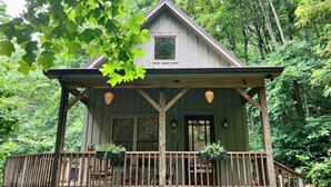 A wooden cabin with a porch, surrounded by trees. - Whimsical Creekside Cabin (Vesuvius)