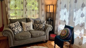 Una sala de estar acogedora con un sofá gris, cojines estampados, piso de madera y un sillón con un cojín de colores.