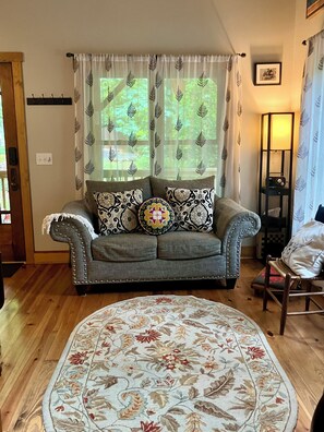 A living room with a grey upholstered sofa, patterned cushions, a round floral rug, and a tall floor lamp. - Whimsical Creekside Cabin (Vesuvius)
