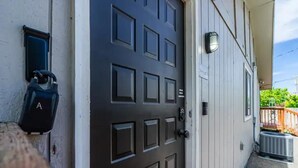 Una porta marrone scuro con serratura a combinazione, una cassetta postale e un piccolo spazio esterno con un pavimento in legno e un portico coperto.