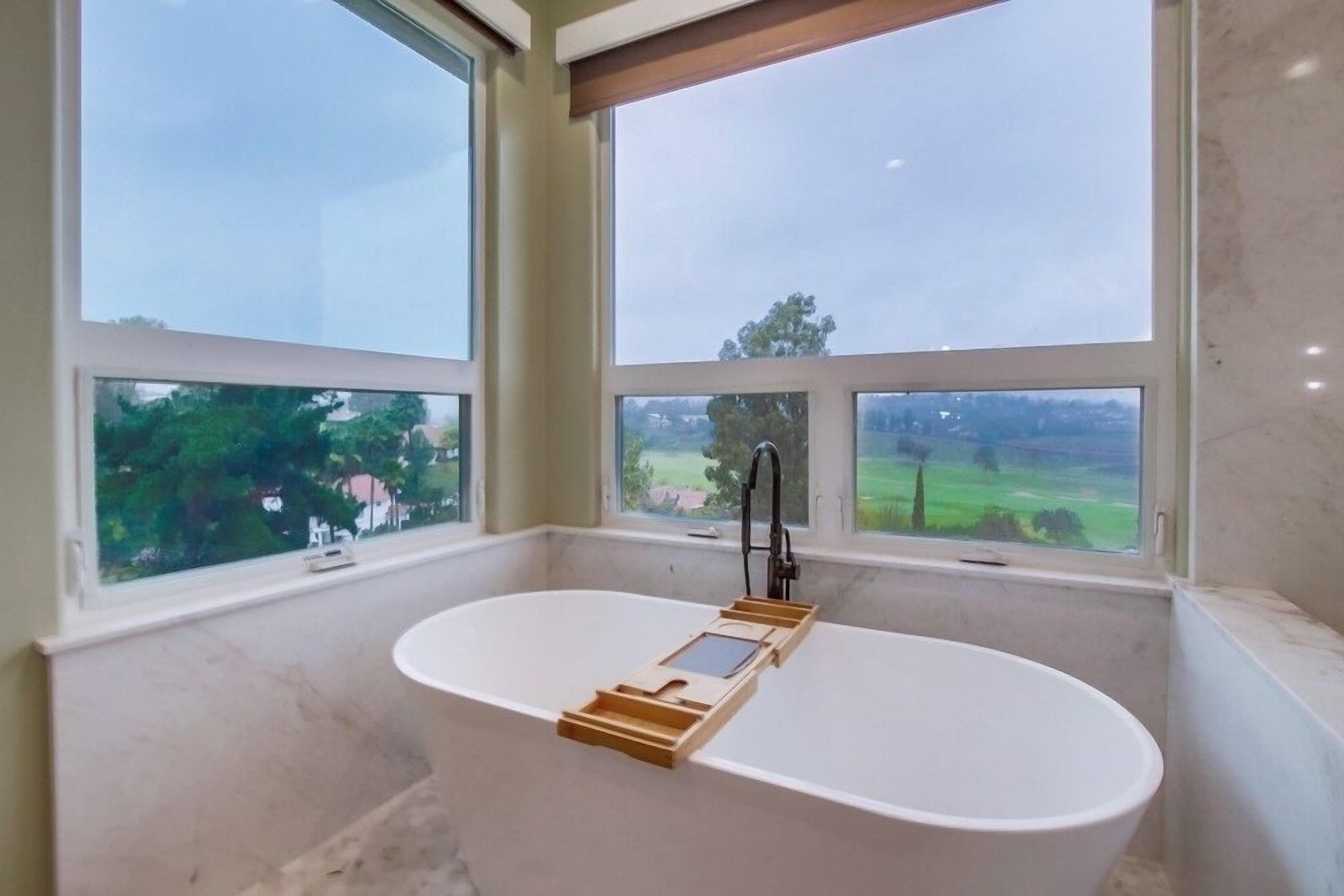 A bathroom with a freestanding bathtub, large windows, and a view of a green landscape.