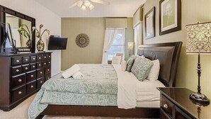 Un dormitorio con cama, cómoda, televisor y ventilador de techo.