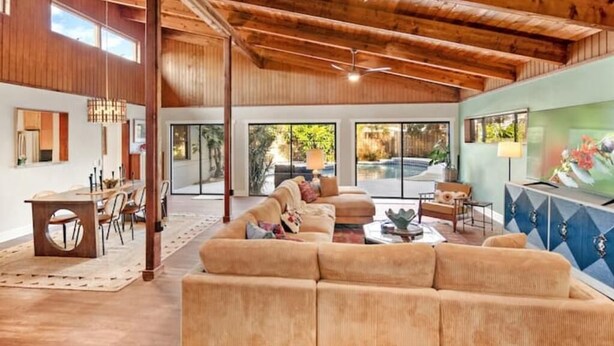 A spacious living area with a wooden ceiling, a large sofa, a dining table with chairs, and a television on the wall. - Mid-mod, boho home w/ a pool! (St. Augustine)