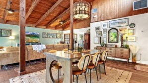 A spacious living area with a wooden ceiling, a dining table with chairs, and a large window overlooking a scenic landscape. - Mid-mod, boho home w/ a pool! (St. Augustine)
